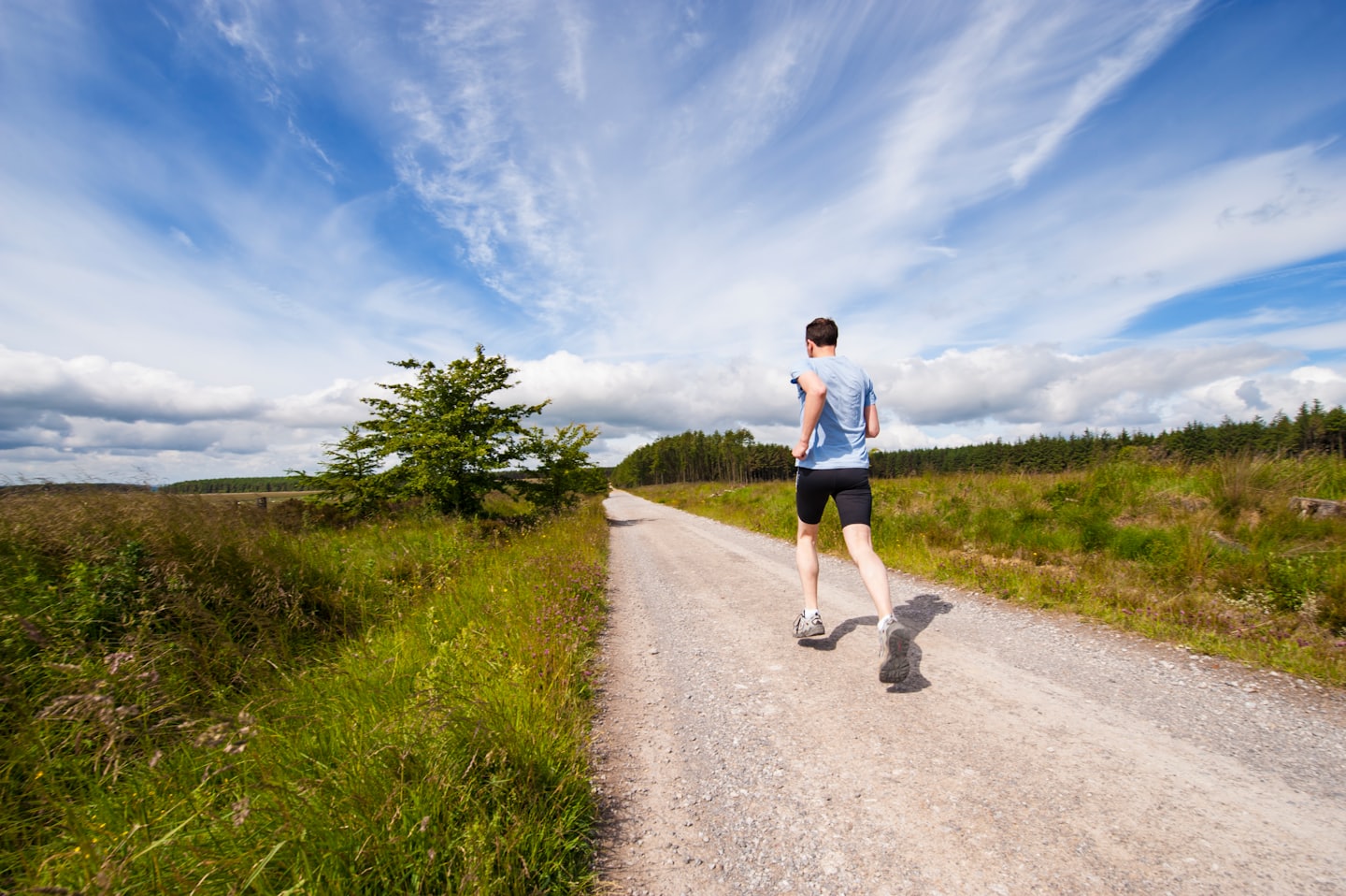 Runner che corre su una strada immersa nel verde sotto un cielo sereno